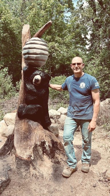 On-site carving — black bear climbing to a beehive, carved in place from an ~8' oak stump in Johnston, RI. Pictured with Mike for scale. Black bear climbing to a beehive, carved from an oak stump, with Mike for scale